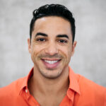 Hispanic man in an orange polo smiles after professional teeth whitening