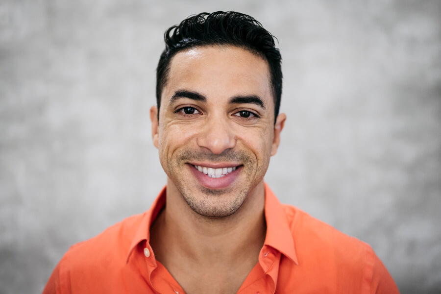 Hispanic man in an orange polo smiles after professional teeth whitening