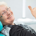senior woman gives a thumbs up in the dentist chair after a full mouth reconstruction