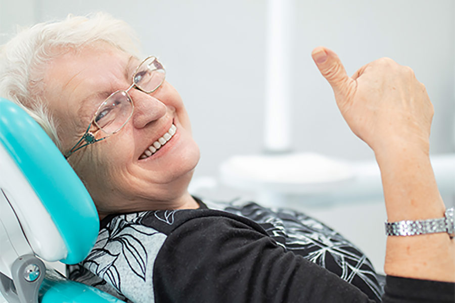 senior woman gives a thumbs up in the dentist chair after a full mouth reconstruction