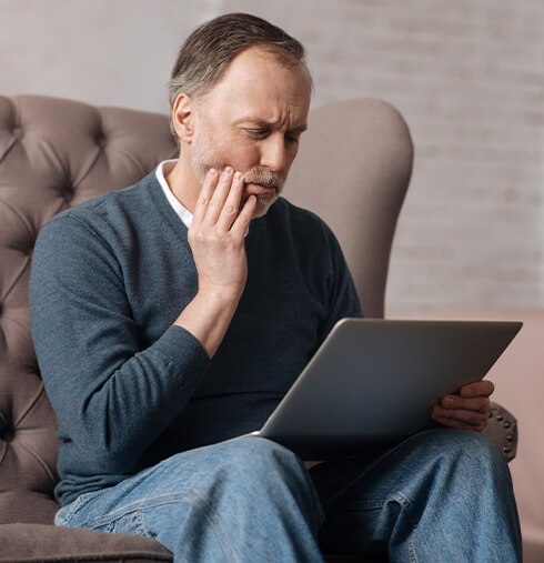 man holding his jaw in pain while looking at his laptop