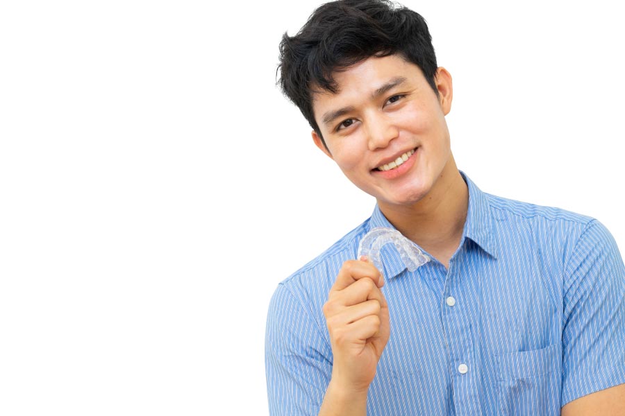 young man holds up his Invisalign clear aligner and smiles